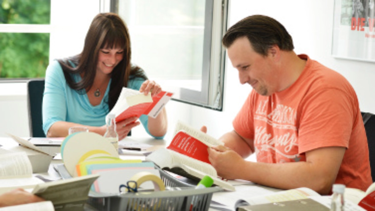 Eine Frau und ein Mann sitzen lächelnd an einem Tisch und lesen in einem Buch.
