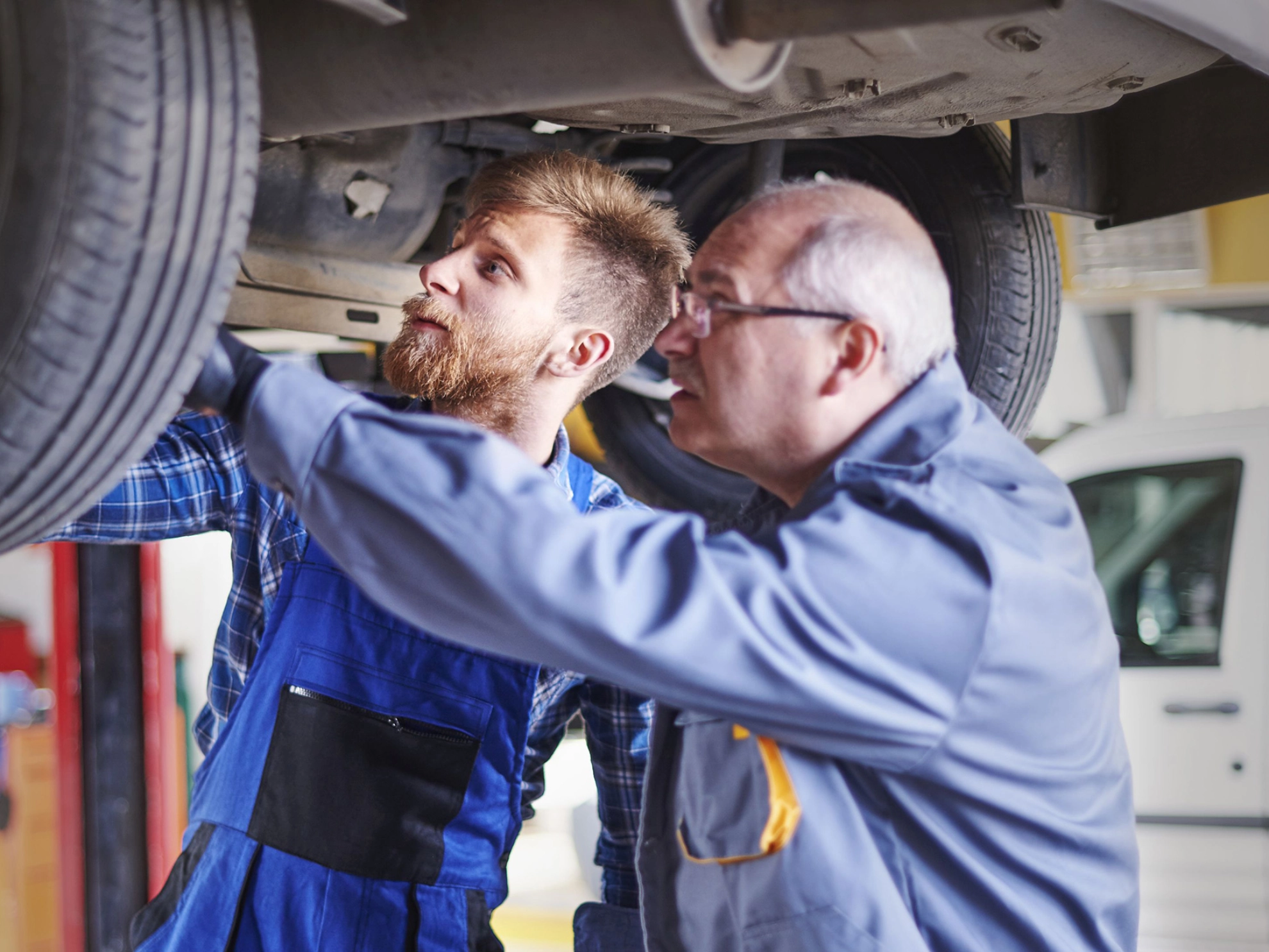 Zwei Kfz-Mechaniker prüfen den Unterboden eines Autos