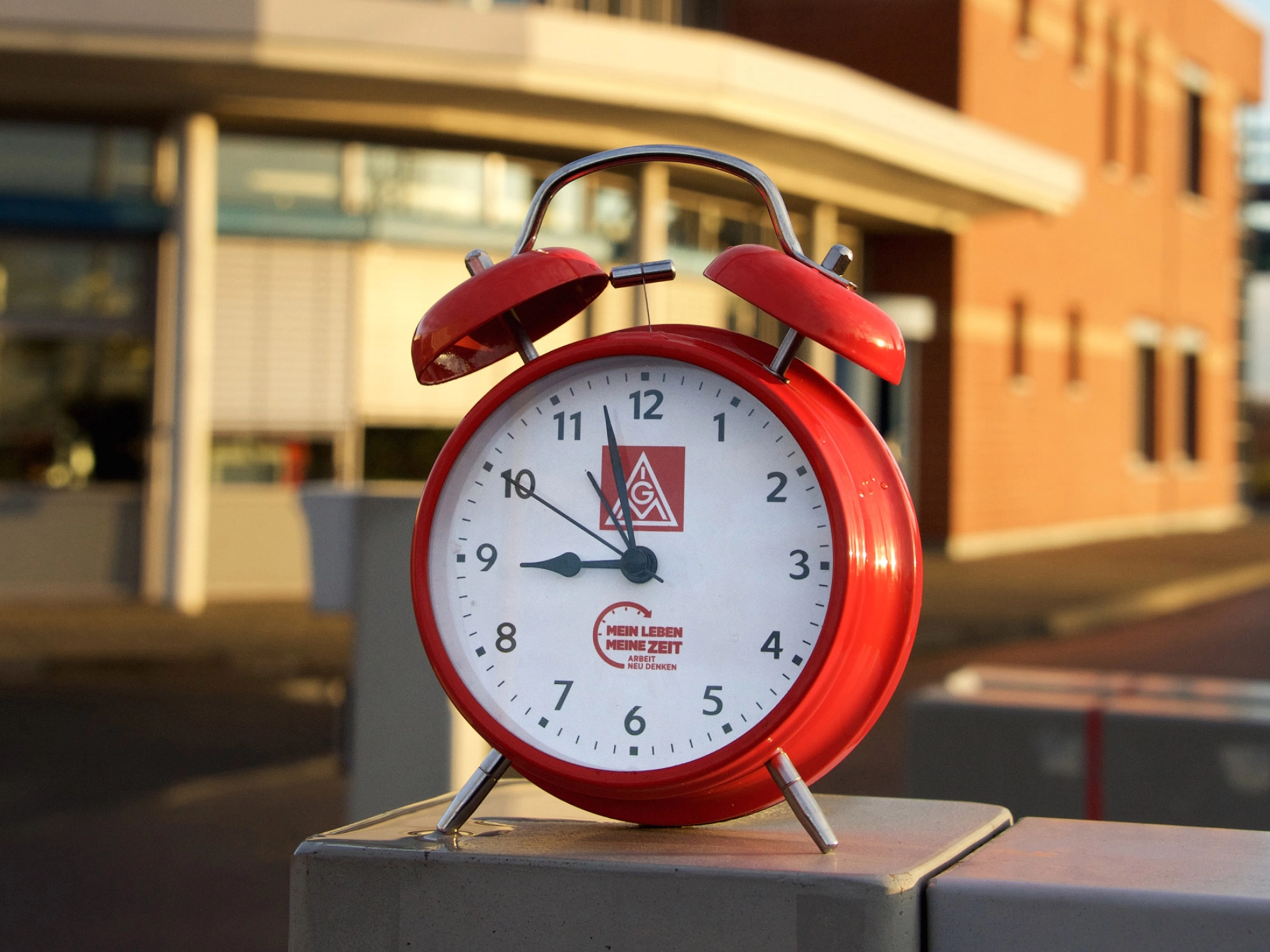 Ein roter Wecker vor einem Industriegebäude.