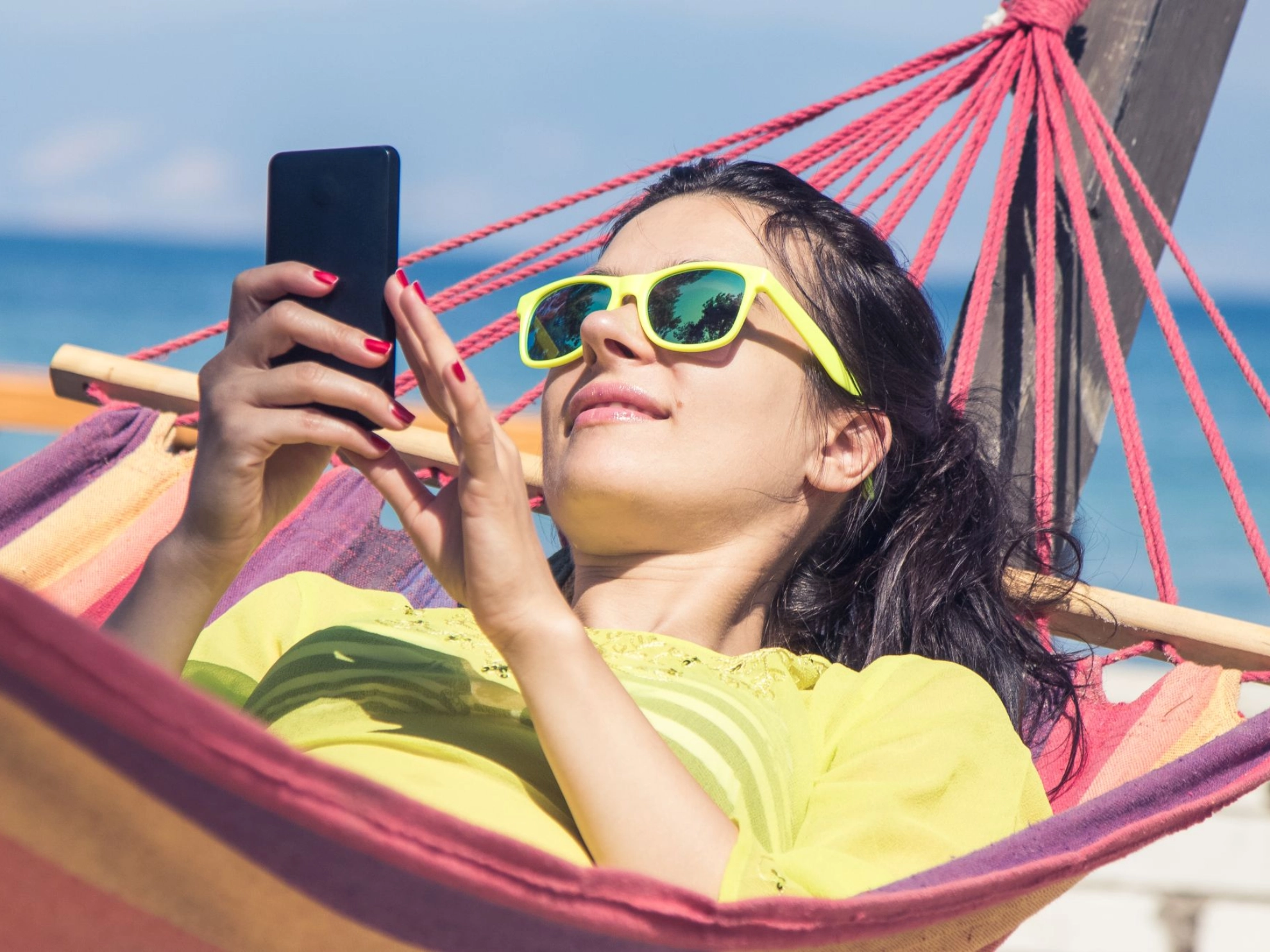 Junge Frau liegt mit ihrem Smartphone in einer Hängematte