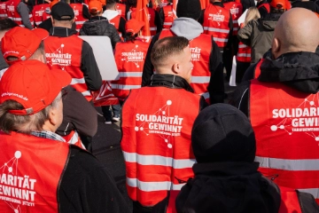 Beschäftigte tragen rote Westen mit dem Aufdruck „Solidarität gewinnt. Tarifbewegung jetzt“ auf dem Rücken