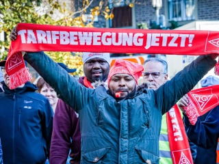 Ein Mann hält einen Schal mit der Aufschrift „Tarifbewegung jetzt“ hoch.